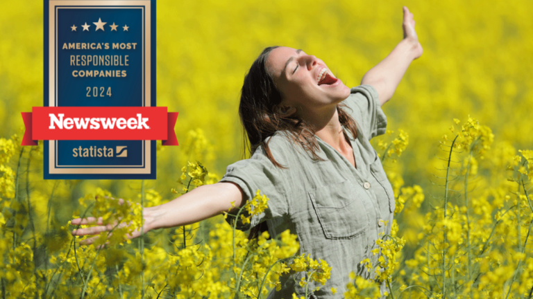 Woman with arms spread and eyes closed in field of flowers.